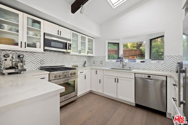 kitchen featuring backsplash, white cabinets, sink, vaulted ceiling with skylight, and appliances with stainless steel finishes