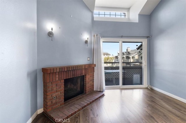 unfurnished living room with a brick fireplace, a wealth of natural light, wood-type flooring, and a towering ceiling