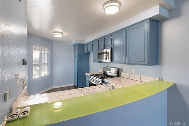 kitchen with blue cabinetry, appliances with stainless steel finishes, and tile counters