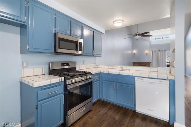 kitchen featuring ceiling fan, blue cabinetry, appliances with stainless steel finishes, and tile counters