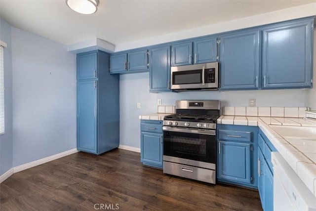 kitchen featuring blue cabinetry, dark hardwood / wood-style flooring, stainless steel appliances, and tile countertops