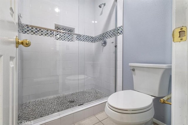 bathroom with toilet, tile patterned floors, and a tile shower