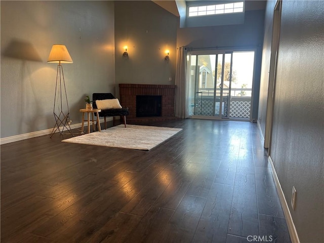 living room with a high ceiling, a brick fireplace, and dark hardwood / wood-style floors