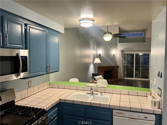 kitchen with tile counters, black range with gas stovetop, blue cabinetry, and white dishwasher