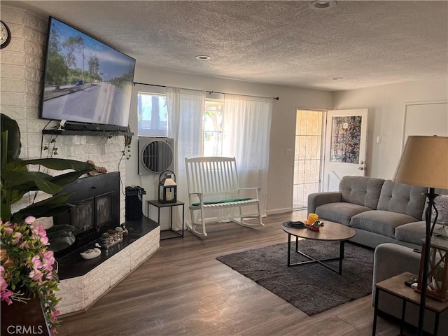 living room with a stone fireplace, a textured ceiling, and hardwood / wood-style flooring