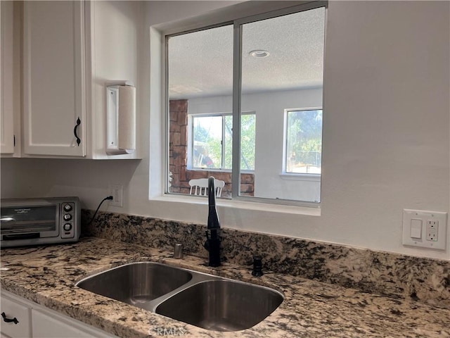 kitchen featuring a textured ceiling, light stone countertops, white cabinetry, and sink