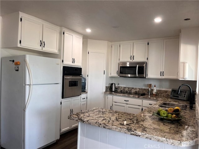 kitchen featuring white cabinets, stainless steel appliances, kitchen peninsula, and light stone counters