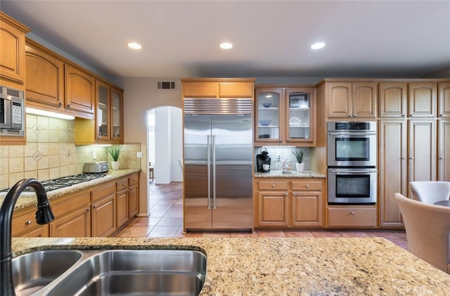 kitchen featuring built in appliances, light stone countertops, and sink