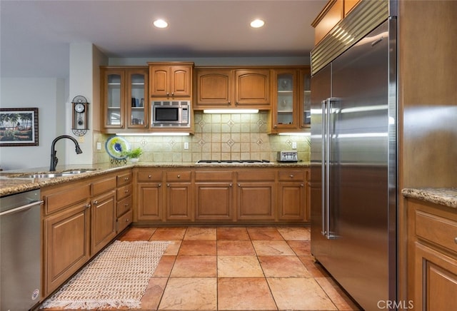 kitchen featuring light stone countertops, decorative backsplash, built in appliances, and sink