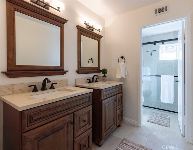 full bath featuring two vanities, visible vents, a tile shower, and a sink