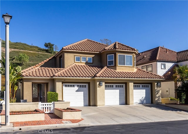 mediterranean / spanish-style home featuring concrete driveway, stucco siding, an attached garage, a tile roof, and fence