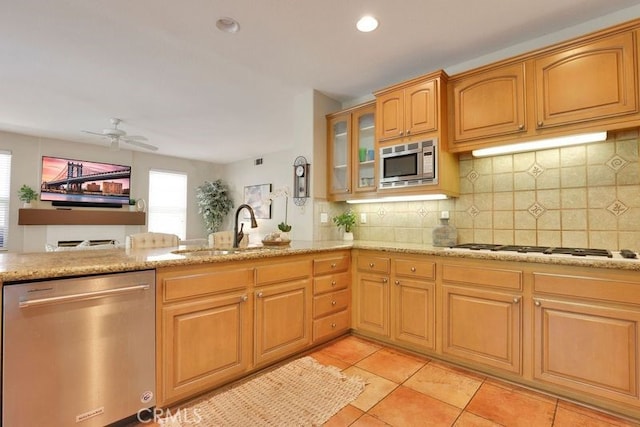 kitchen with glass insert cabinets, appliances with stainless steel finishes, light stone counters, a sink, and backsplash