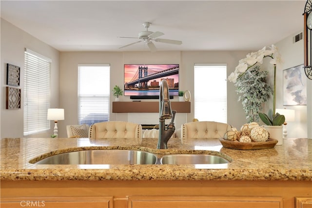 kitchen with visible vents, a ceiling fan, a sink, and light stone counters