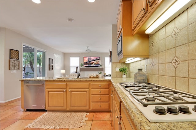 kitchen with stainless steel dishwasher, light tile patterned floors, tasteful backsplash, a peninsula, and white gas stovetop