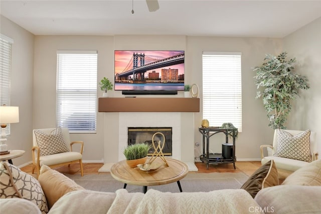 living room with a tiled fireplace, a ceiling fan, baseboards, and a wealth of natural light