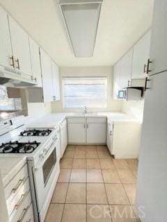 kitchen with exhaust hood, white cabinetry, light tile patterned floors, and white range with gas stovetop