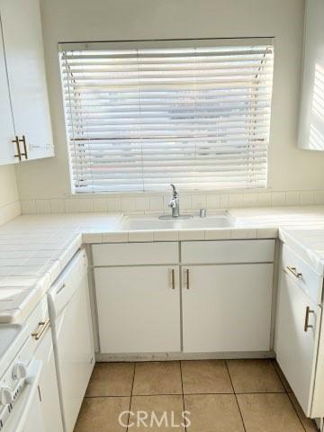 kitchen with light tile patterned flooring, white cabinetry, white dishwasher, and a sink