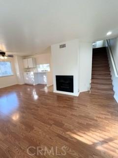 unfurnished living room with ceiling fan, stairway, wood finished floors, and a fireplace