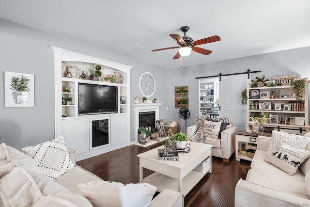 living room featuring ceiling fan, a barn door, and dark wood-type flooring