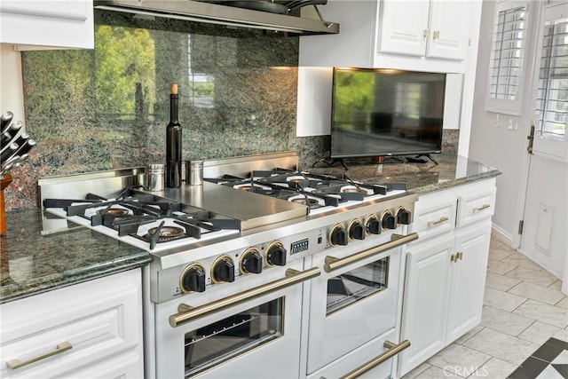 kitchen featuring white cabinetry, dark stone countertops, backsplash, double oven range, and exhaust hood