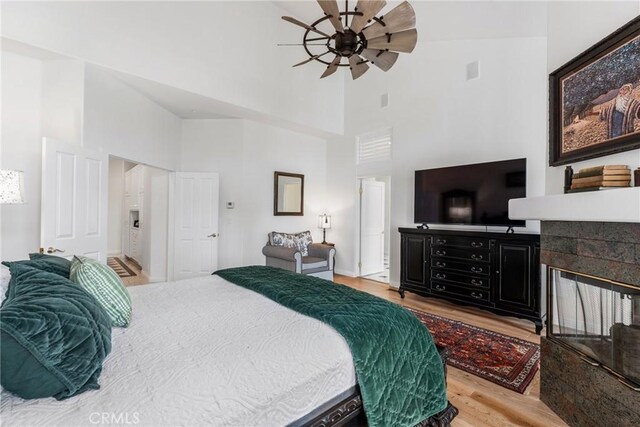 bedroom featuring a tiled fireplace, high vaulted ceiling, ceiling fan, and light wood-type flooring