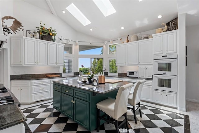 kitchen featuring white cabinetry, white appliances, a breakfast bar, and a skylight