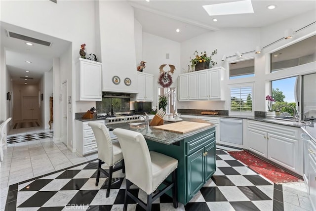 kitchen featuring a skylight, sink, white cabinets, a kitchen breakfast bar, and a kitchen island with sink