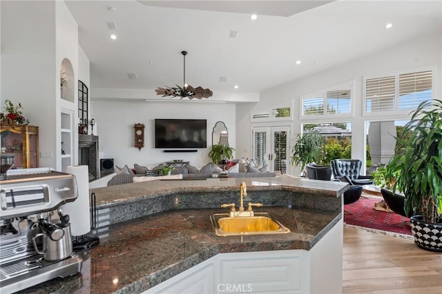 kitchen featuring sink, light hardwood / wood-style flooring, dark stone countertops, white cabinets, and decorative light fixtures