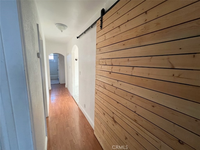 hallway featuring a barn door, wooden walls, and light hardwood / wood-style flooring