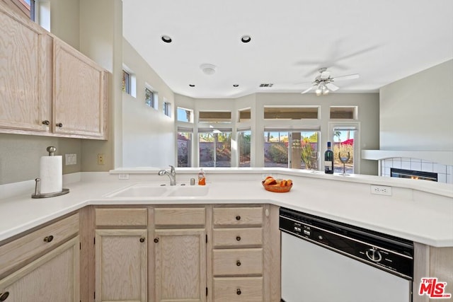 kitchen with white dishwasher, sink, light brown cabinetry, kitchen peninsula, and a tiled fireplace