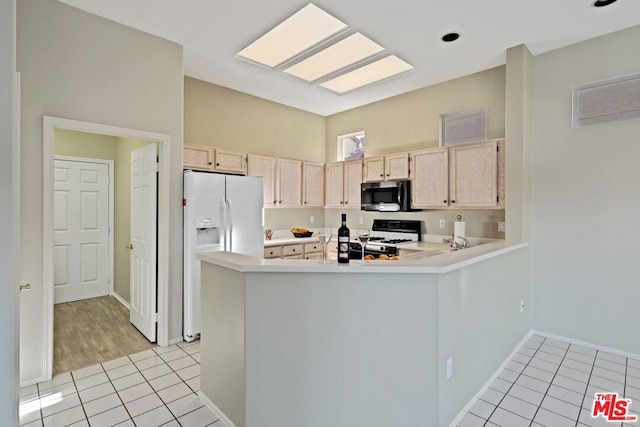 kitchen with white appliances, kitchen peninsula, light brown cabinetry, and a skylight