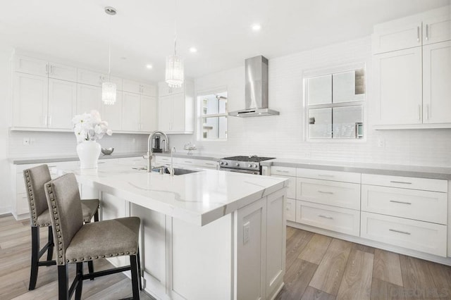 kitchen with white cabinets, an island with sink, stainless steel range, and wall chimney range hood