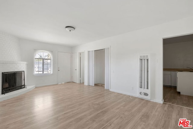 unfurnished living room featuring a brick fireplace, sink, and light hardwood / wood-style flooring