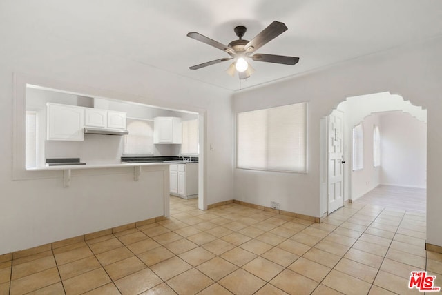 kitchen with ceiling fan, light tile patterned flooring, kitchen peninsula, a breakfast bar area, and white cabinets