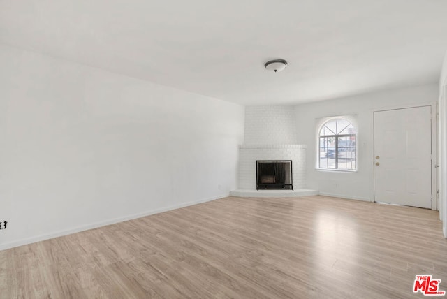 unfurnished living room with light hardwood / wood-style floors and a brick fireplace