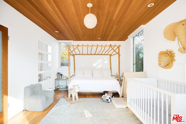 bedroom with hardwood / wood-style flooring, a nursery area, wooden ceiling, and multiple windows