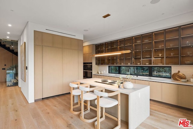 kitchen featuring hanging light fixtures, a kitchen island, backsplash, and light hardwood / wood-style flooring