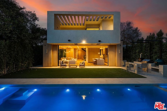 back house at dusk with an outdoor kitchen, an outdoor hangout area, a patio, and a lawn