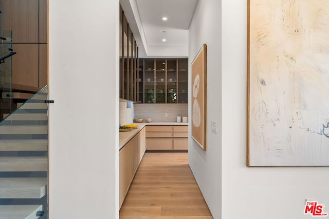 bar with light brown cabinets, backsplash, and light hardwood / wood-style flooring