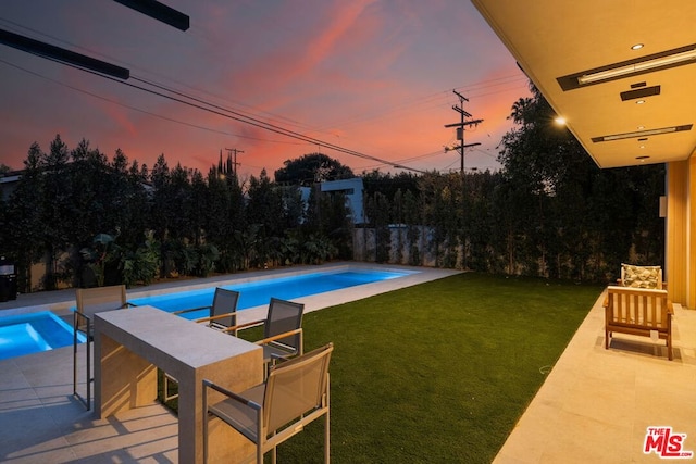 pool at dusk featuring a patio and a lawn