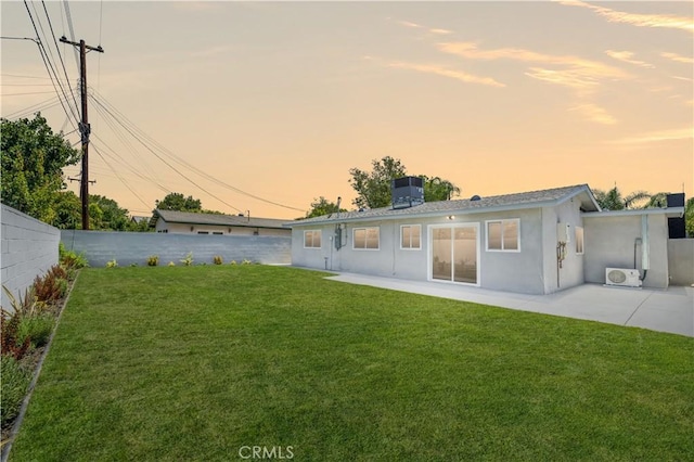 back house at dusk featuring a lawn, a patio area, ac unit, and cooling unit