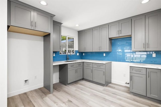 kitchen featuring decorative backsplash, light wood-type flooring, gray cabinetry, and sink