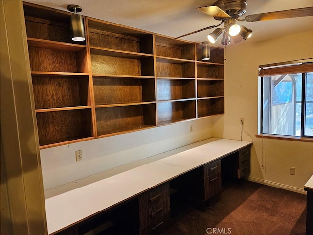 unfurnished office featuring ceiling fan, built in desk, and dark carpet