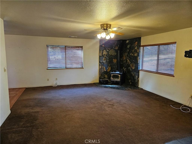 unfurnished living room with carpet, ceiling fan, a wood stove, and a textured ceiling