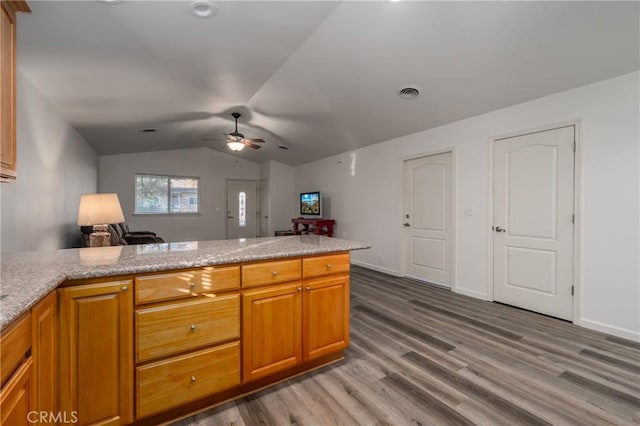 kitchen featuring kitchen peninsula, light stone countertops, vaulted ceiling, ceiling fan, and wood-type flooring