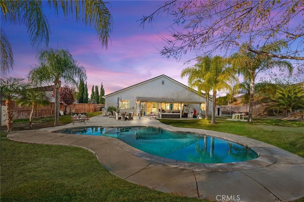 pool at dusk featuring a lawn and a patio area