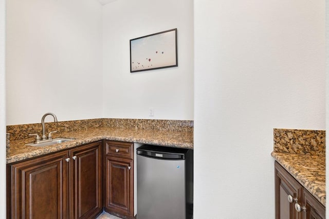 kitchen featuring dark brown cabinetry, stainless steel fridge, sink, and light stone counters