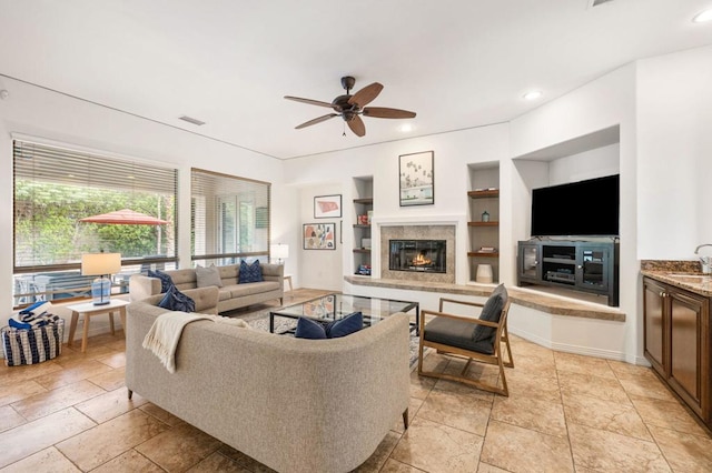 living room with sink, built in features, ceiling fan, and a tiled fireplace