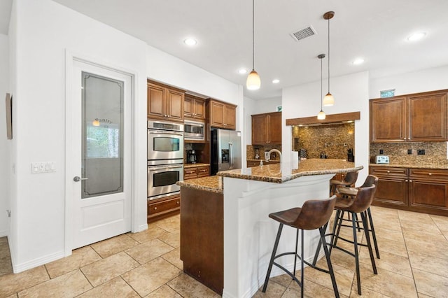 kitchen featuring backsplash, a kitchen island with sink, decorative light fixtures, a kitchen bar, and stainless steel appliances