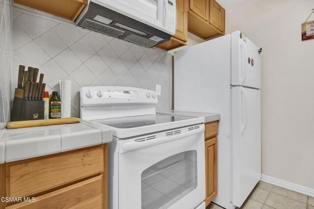 kitchen with tile counters, decorative backsplash, white appliances, and light tile patterned floors